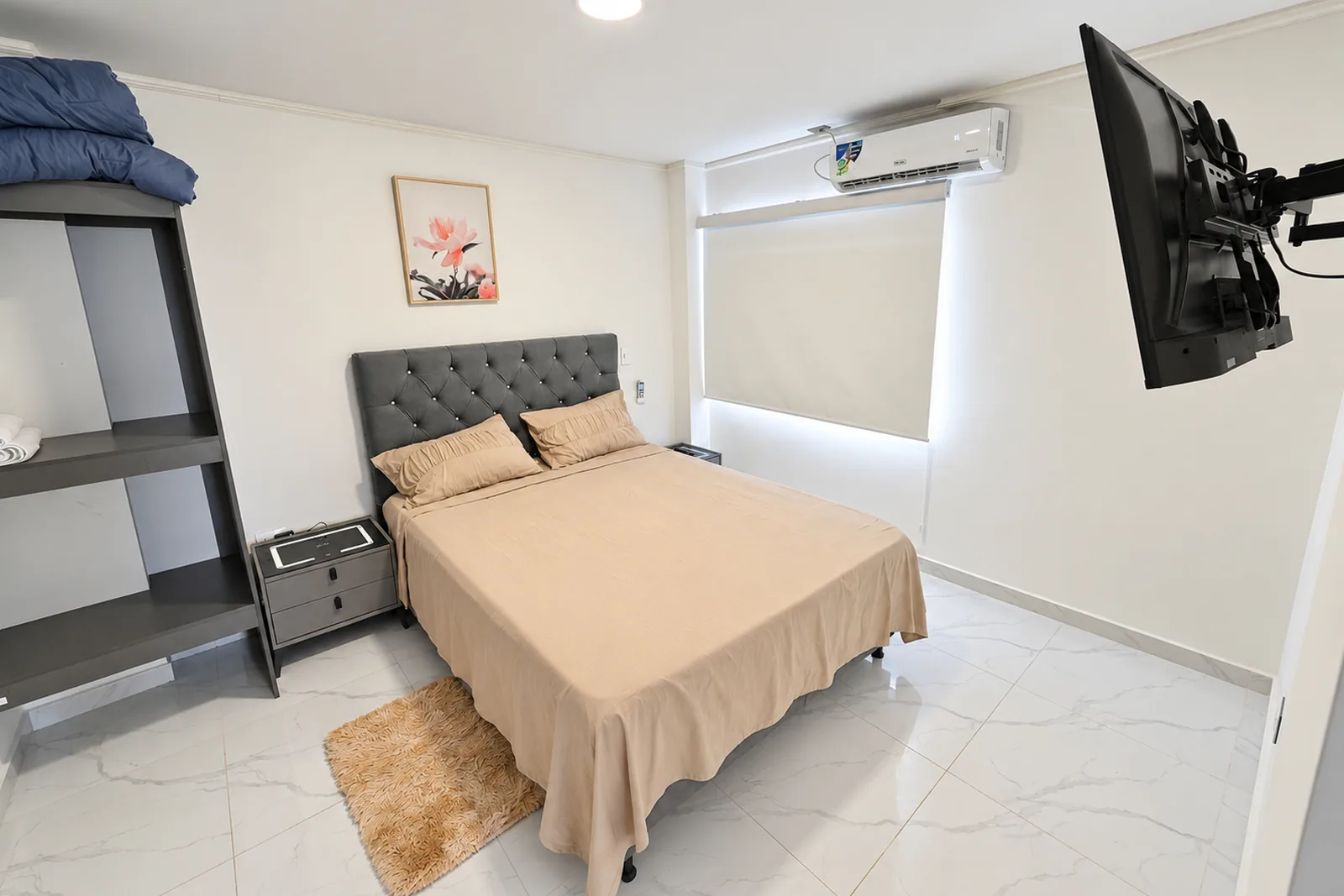 Una de las dos habitaciones del apartamento, con cama doble, televisor y un estante abierto con toallas.